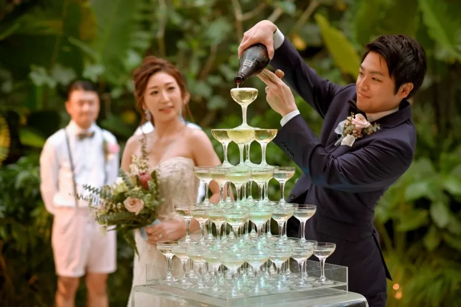 The groom pours champagne into glasses during their wedding reception in Bali