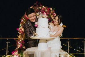 Couple cutting wedding cake on the glass stage at Tirtha Uluwatu.