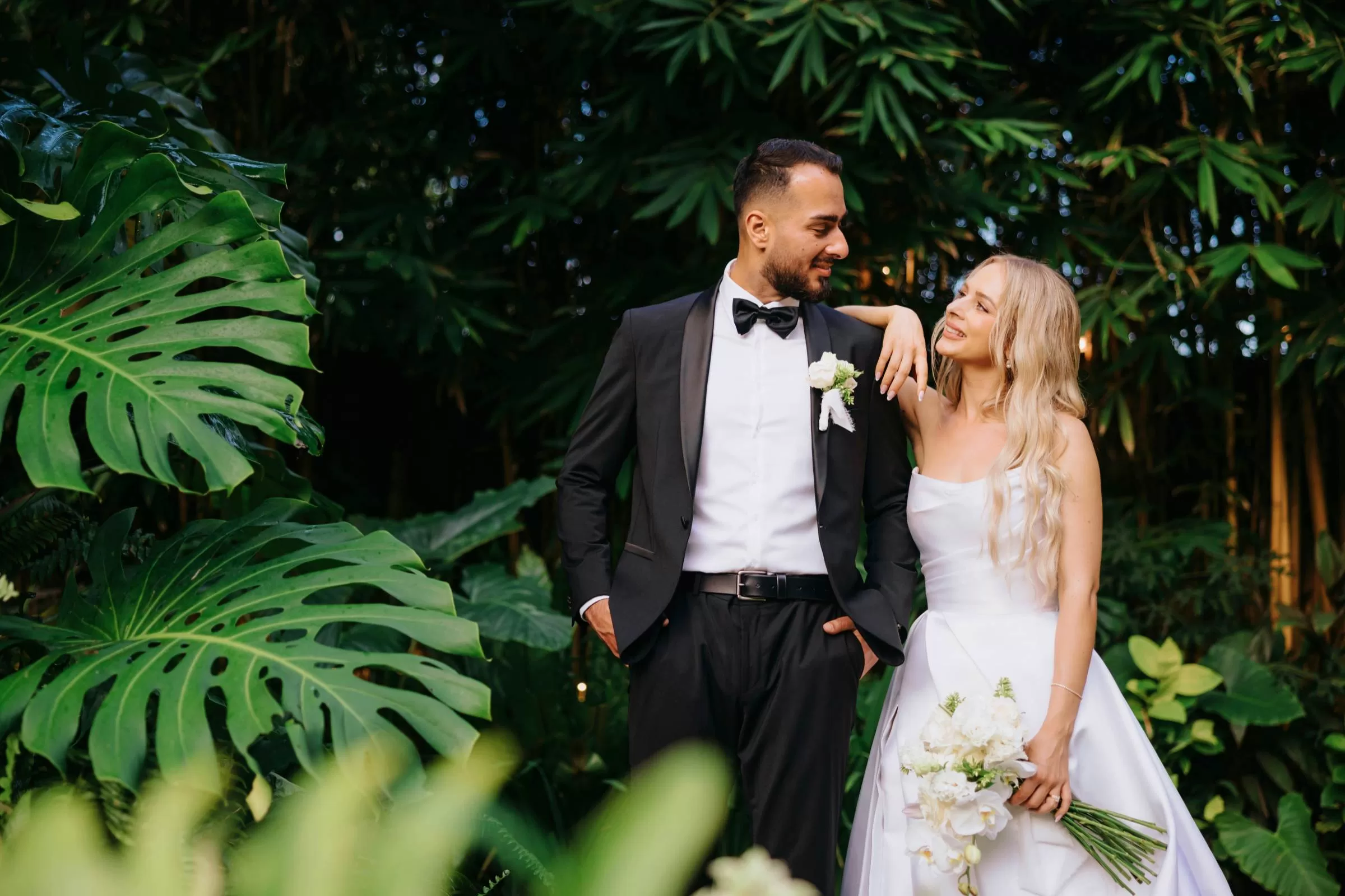 A romantic moment between the bride and groom amid tropical greenery at the Glass House by Tirtha.