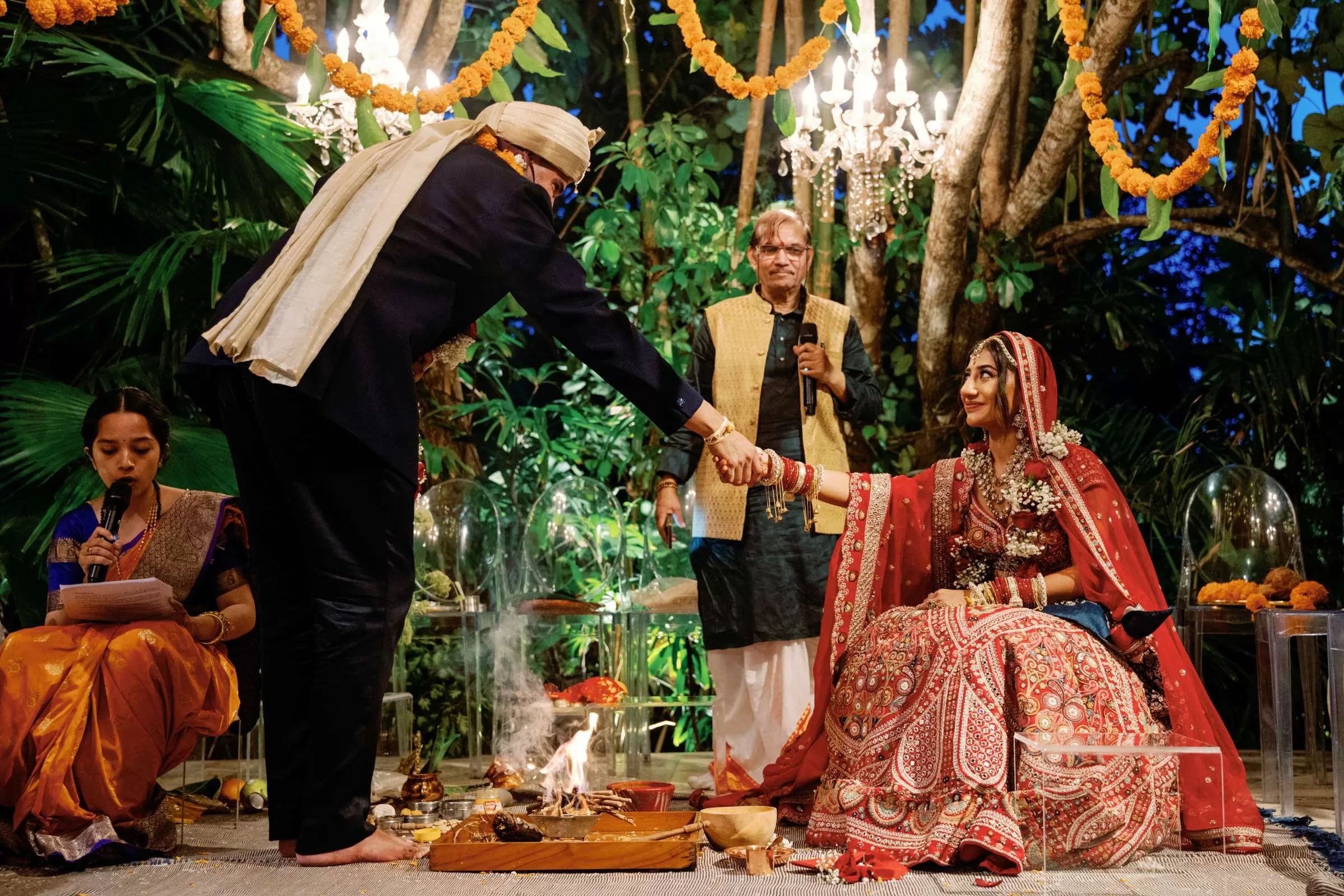 Indian wedding ceremony at Moonlight Garden with bride seated as groom holds her hand across the sacred fire.