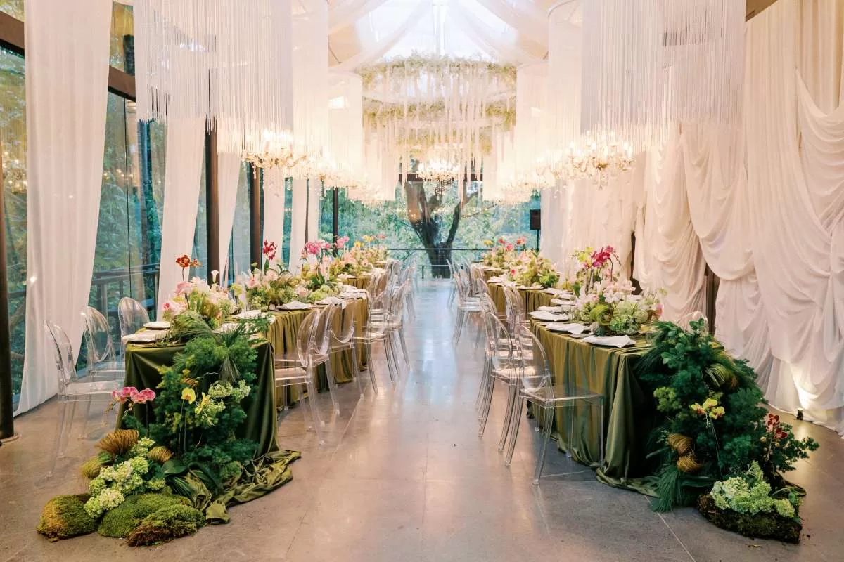 Dinner reception set up at the Plumeria Room, decorated with crystal fringe chandeliers, white drapery, and vibrant florals.