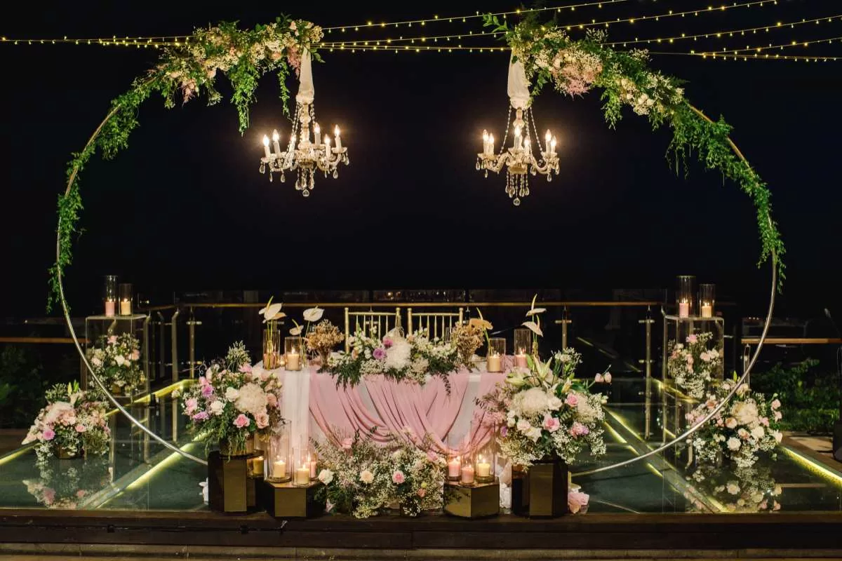Wedding reception setup featuring a chandelier with greenery stand and sweetheart table at Tirtha Uluwatu's Glass Stage.