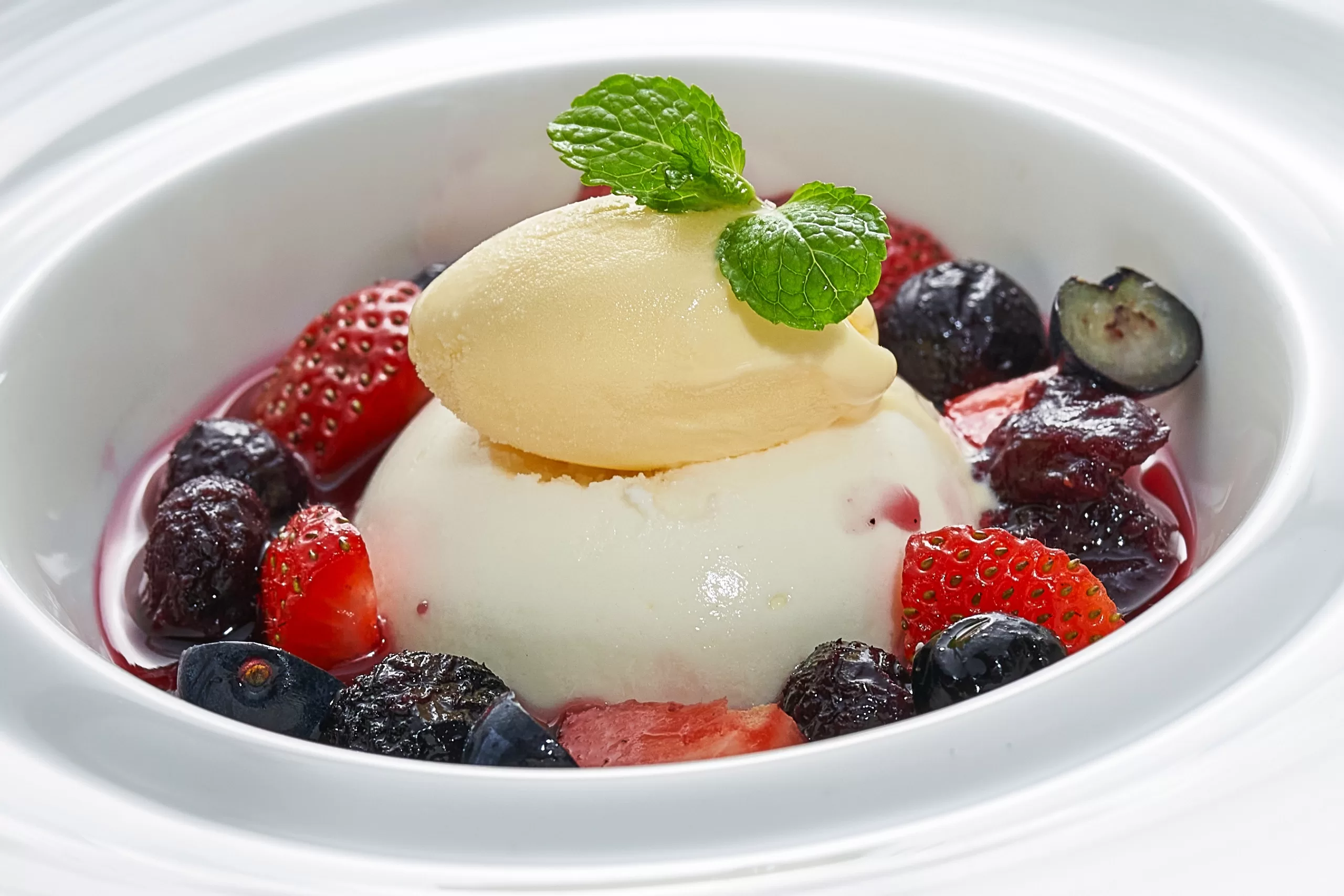 Fromage blanc mousse with aromatic rose syrup served in red berry soup and garnished with mint leaves.