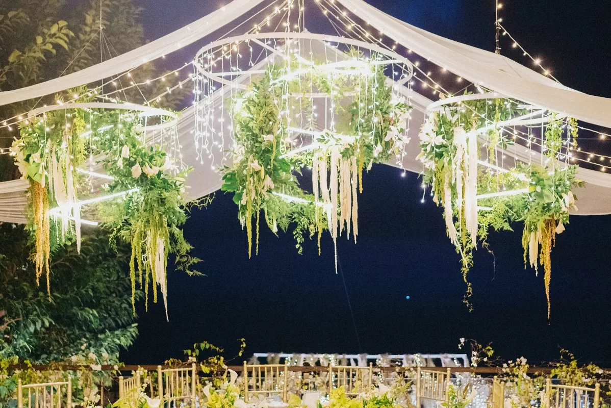 Wedding reception lighting setup with spiral chandeliers adorned with greenery and LED lights at Tirtha Bali.