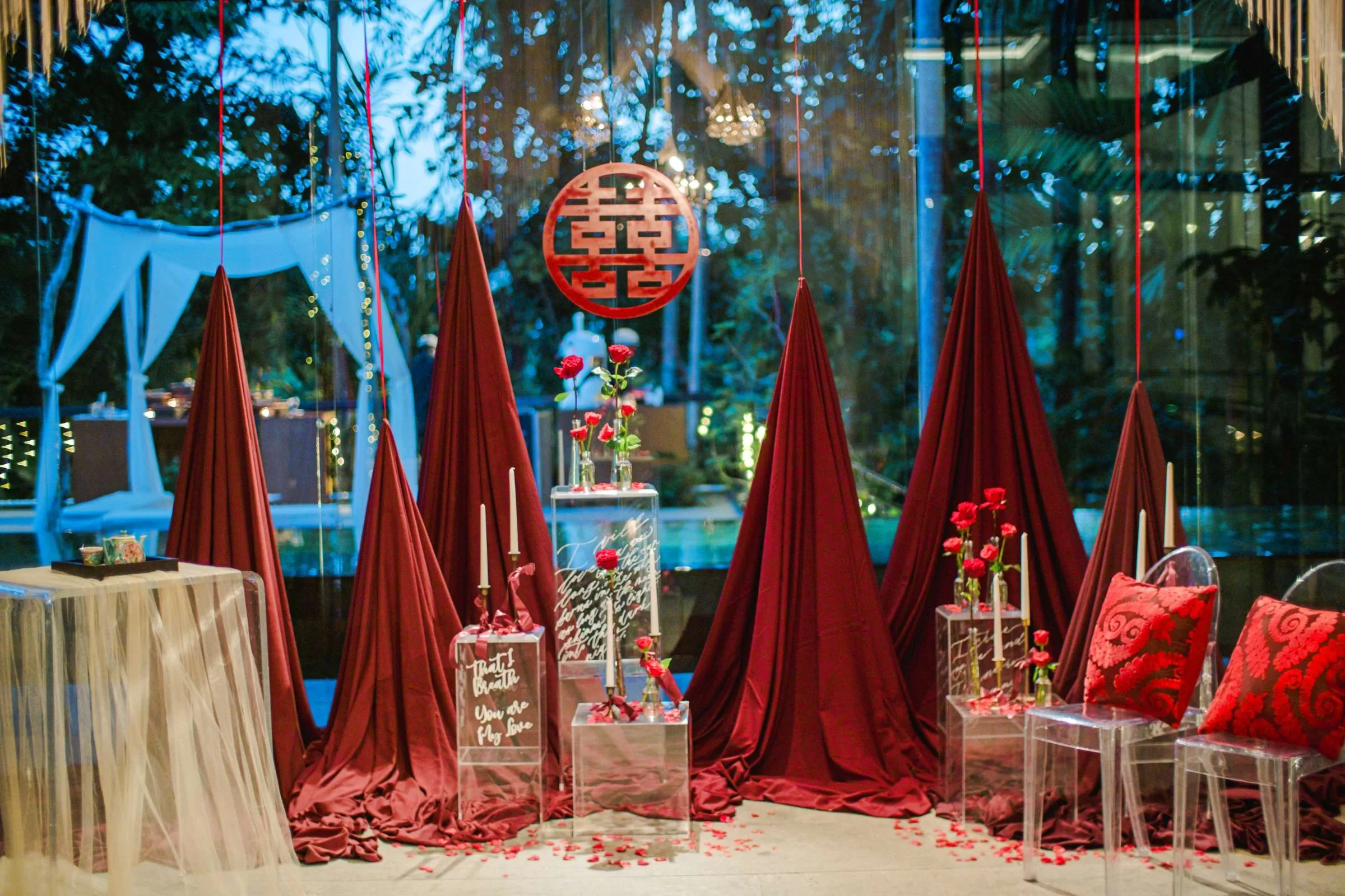 Chinese tea ceremony wedding decorations with red draped backdrop, roses, and candlelight at Tirtha Bali.
