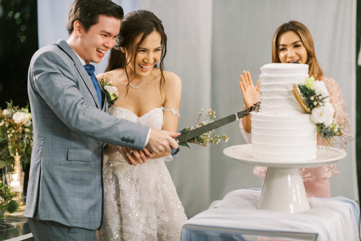 In the Plumeria Room, the couple shares a sweet moment cutting their wedding cake as guests look on.