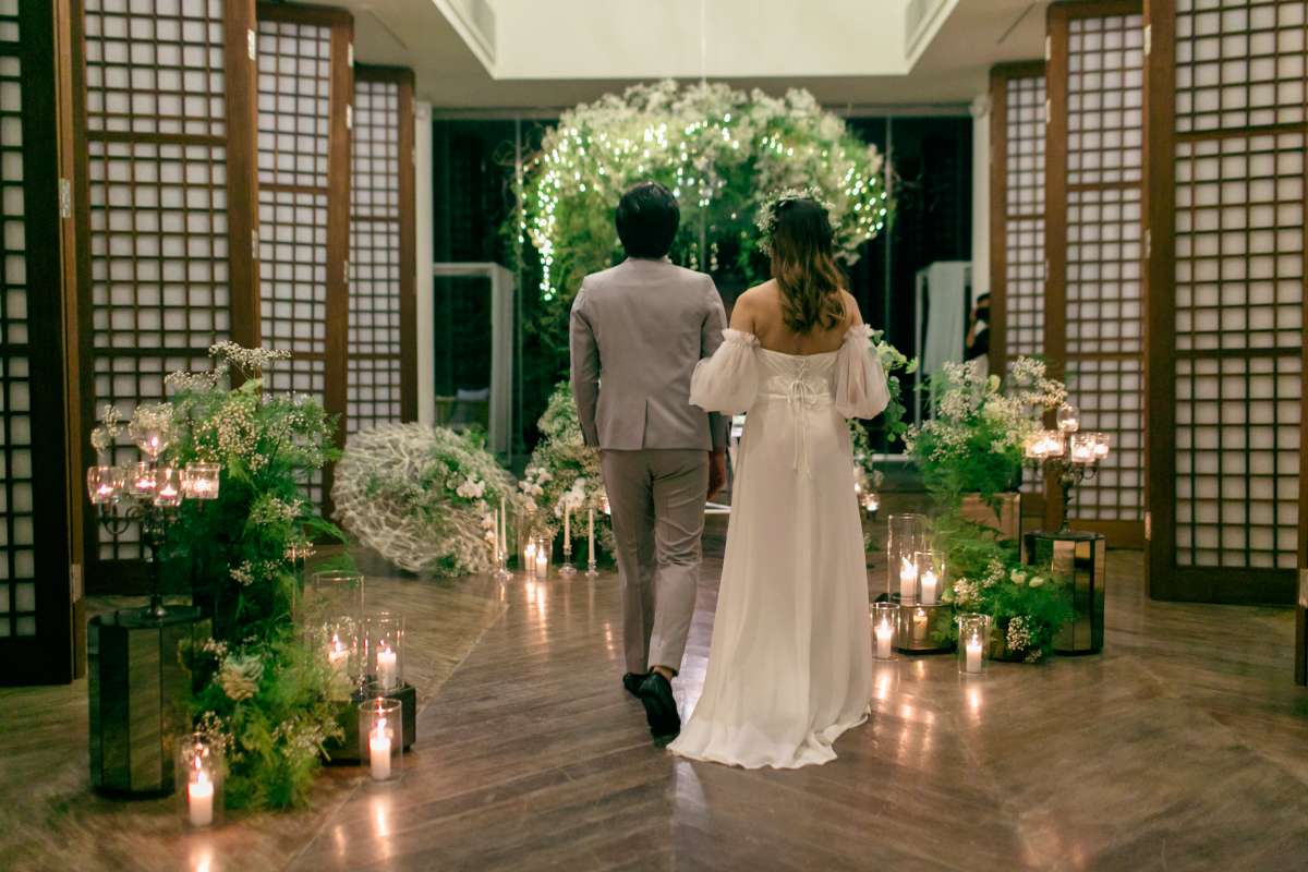 The couple walks hand in hand into a candlelit, botanical reception in the Heaven Room at Tirtha Uluwatu.