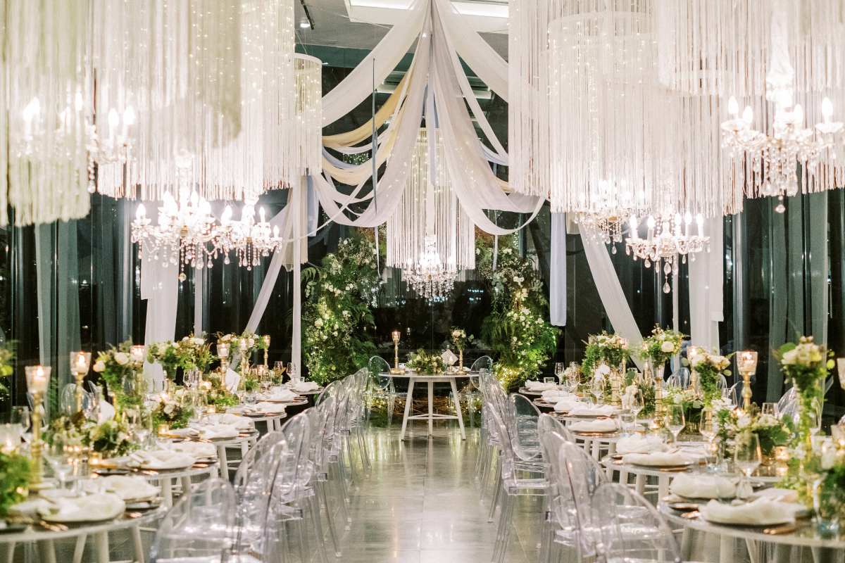 Reception in the Plumeria Room, where lush greenery and chandeliers glow within glass walls.