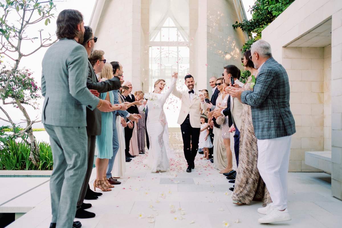Just married couple exits Tirtha Uluwatu's Glass Chapel surrounded by guests at their Bali destination wedding.