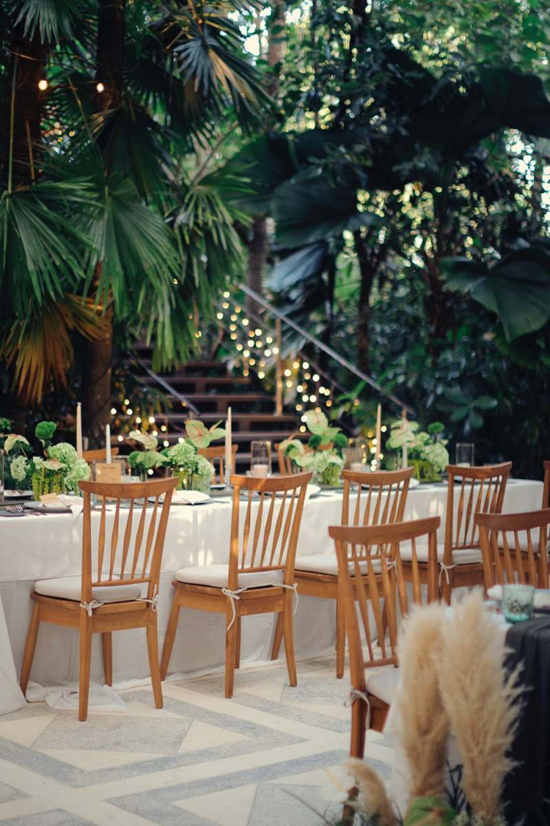 Reception venue setup with long tables, green centerpieces, and palm backdrop for a Bali destination wedding.