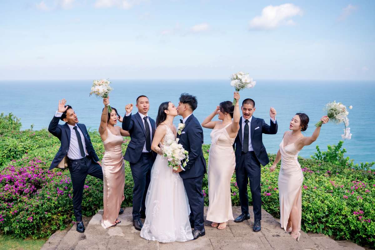 Couple celebrating with bridesmaids and groomsmen at Tirtha Uluwatu, overlooking the ocean.