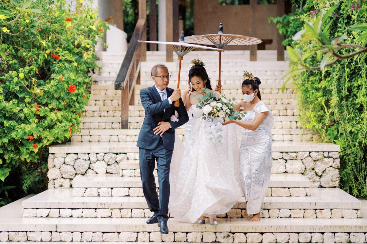 Bride escorted down stone steps at Tirtha Uluwatu, a serene Bali wedding venue.