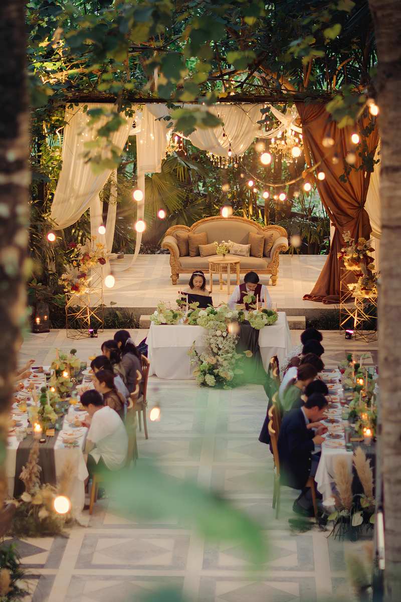 Long dining tables elegantly styled under fairy lights for a bali wedding reception at Tirtha garden venue.