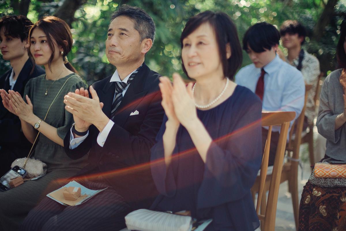 Parents clap with heartfelt emotion during the wedding ceremony beneath the trees at Tirtha Bali.