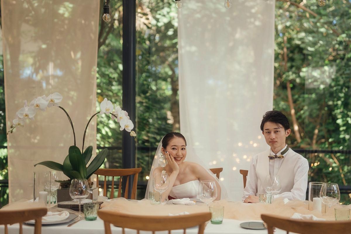 Wedding couple seated at decorated dining table surrounded by orchids and natural light.