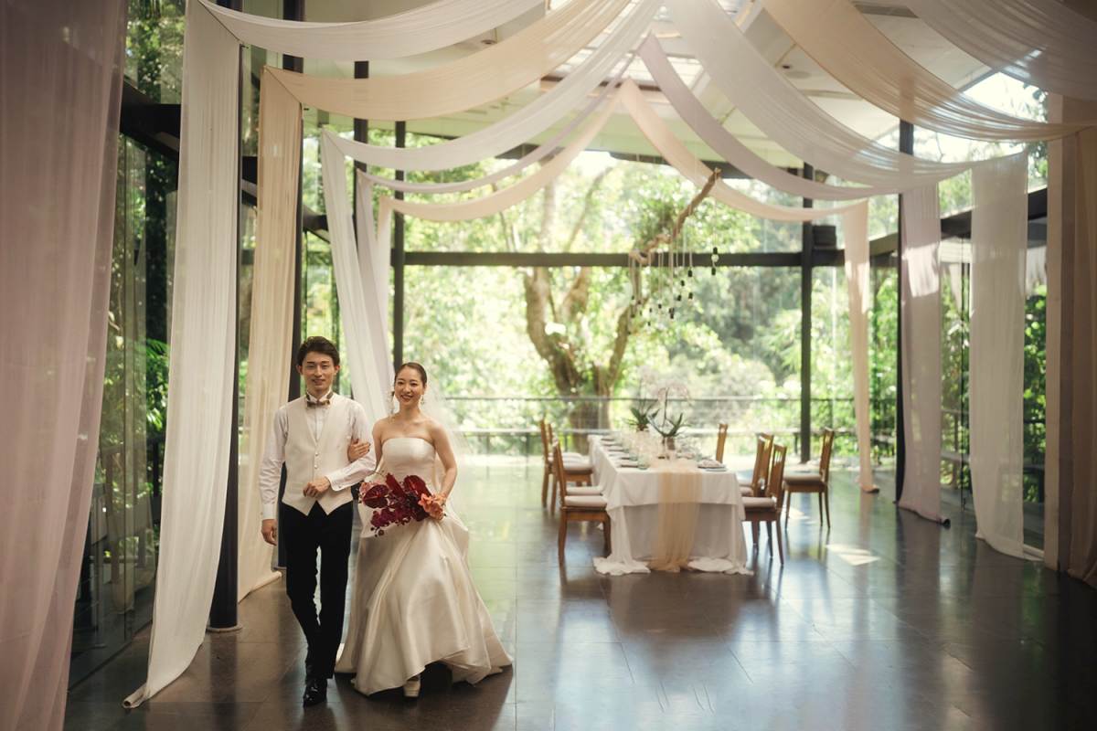 Bride and groom walk through the wedding reception hall adorned with flowing white drapes.