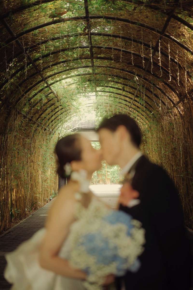 Romantic blurred kiss moment under lush vine tunnel at the Glass House by Tirtha.