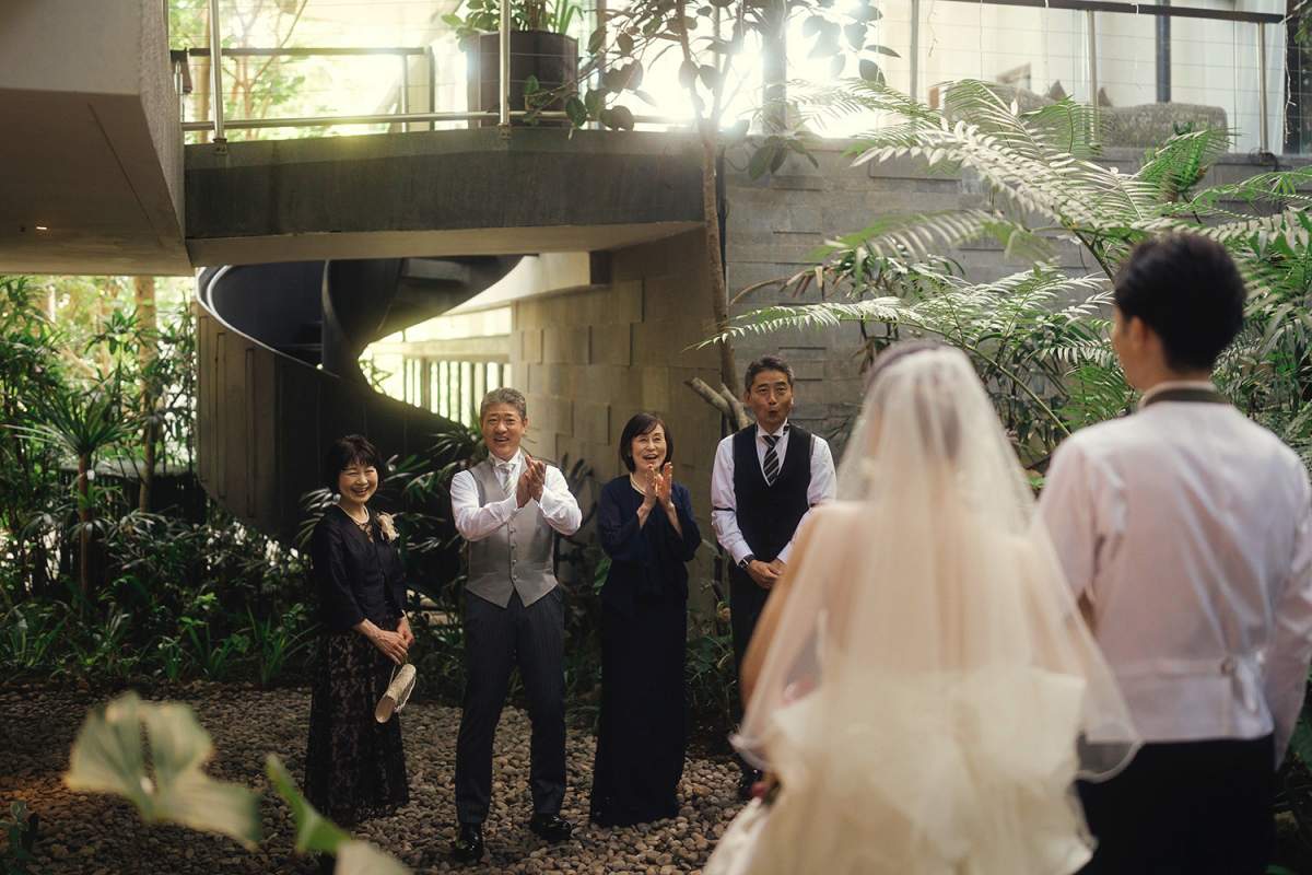Family clapping and smiling as bride and groom arrive for a surprise proposal moment.