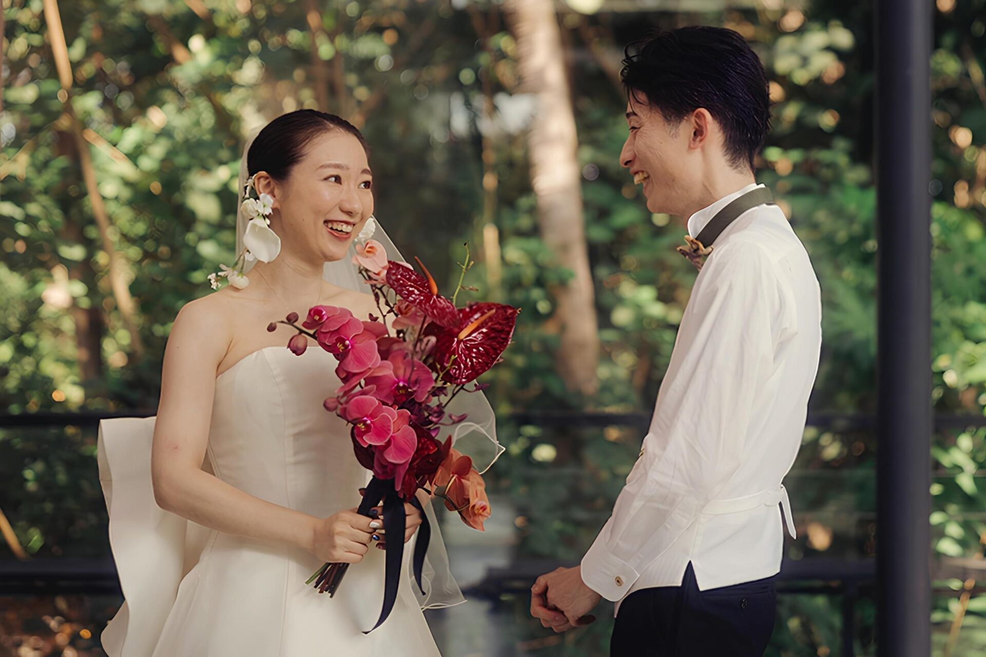 Bride and groom smiling at each other during their Bali destination wedding at Tirtha, holding a vibrant orchid bouquet.