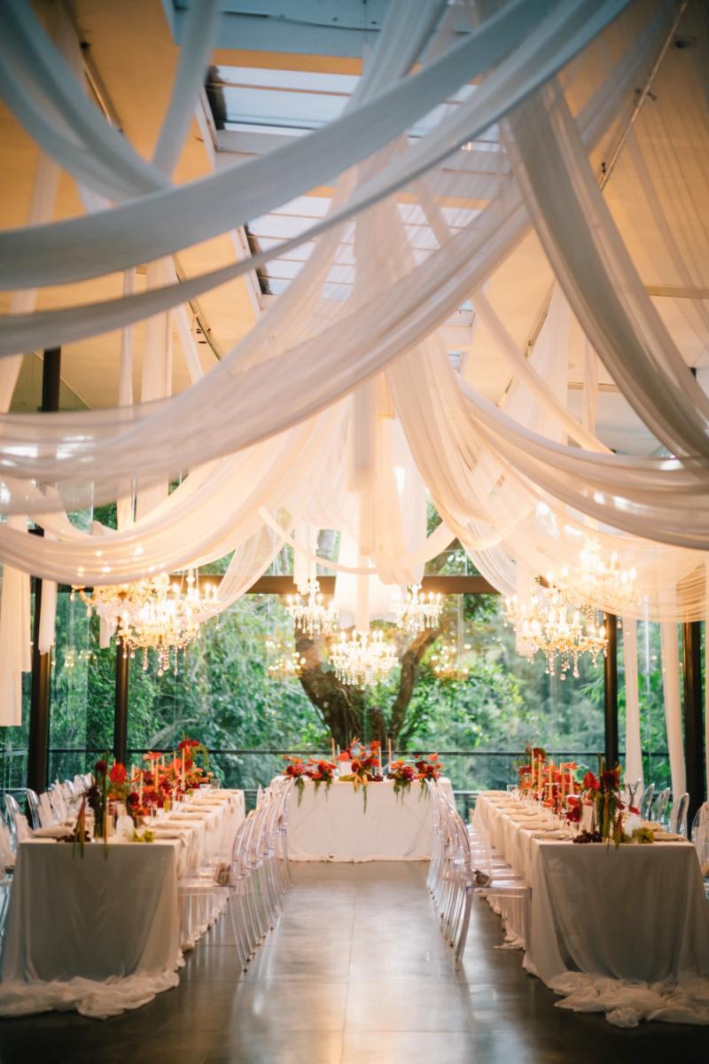 Romantic indoor wedding reception in the Plumeria Room, styled with draped fabric and chandeliers.