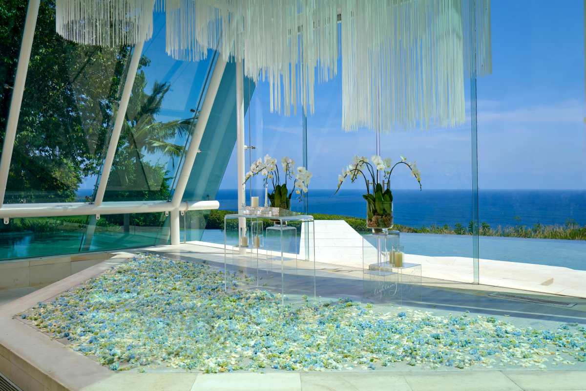 Sunlit glass chapel wedding venue in Bali with ocean backdrop at Tirtha Uluwatu.