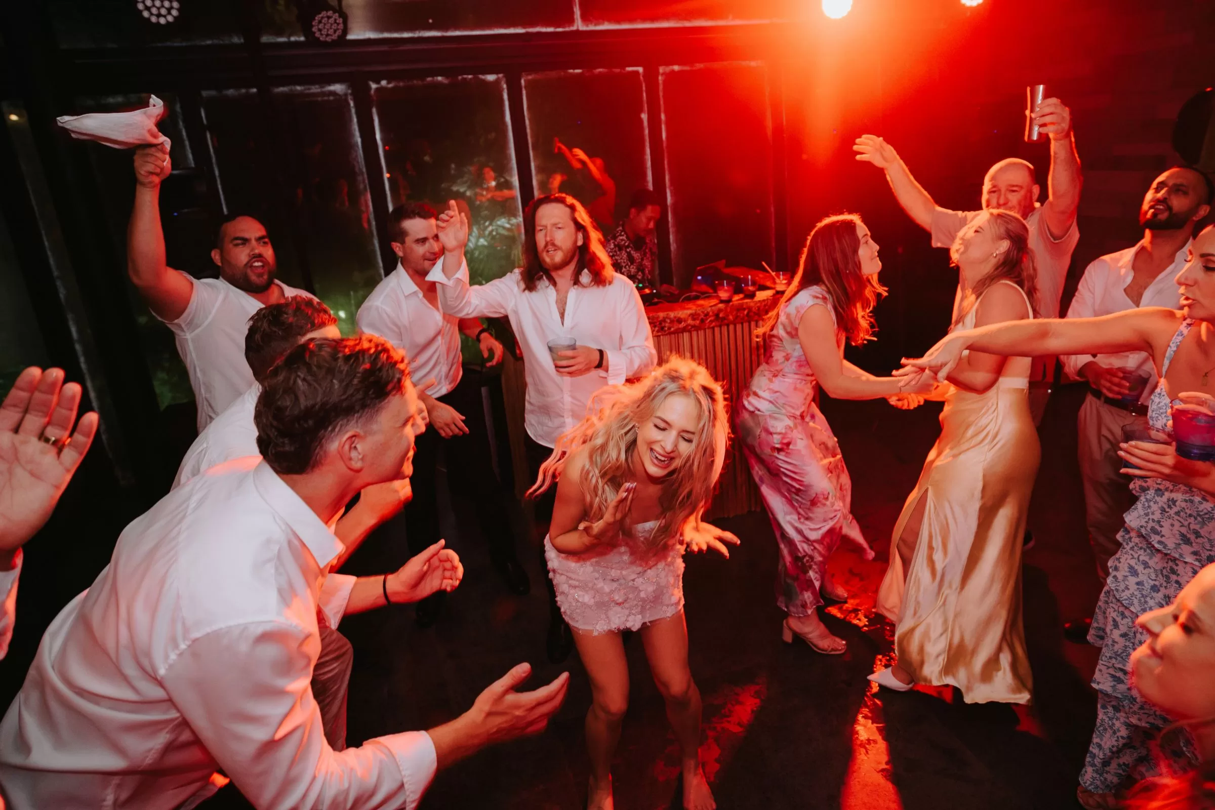 Bride and guests dancing joyfully under red lighting during a wedding after-party at Tirtha Bali.
