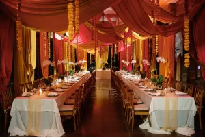 Indian Hindu wedding reception decor with long tables, pink and yellow drapes, and marigold garlands at the Plumeria Room.