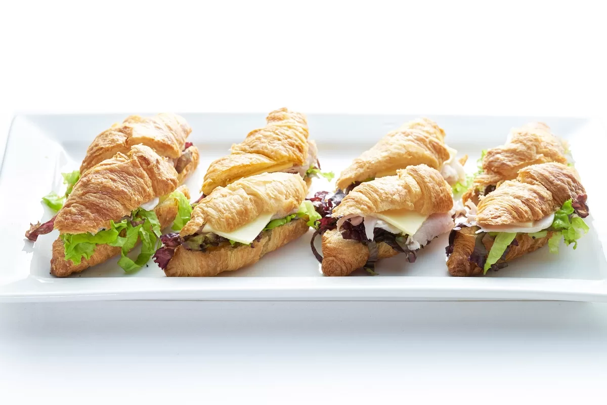 Croissant sandwich with flaky pastry filled with ham, cheese, and fresh vegetables.