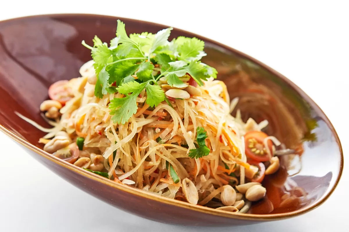 Green papaya salad with shredded papaya, peanuts, and cherry tomatoes, garnished with cilantro.