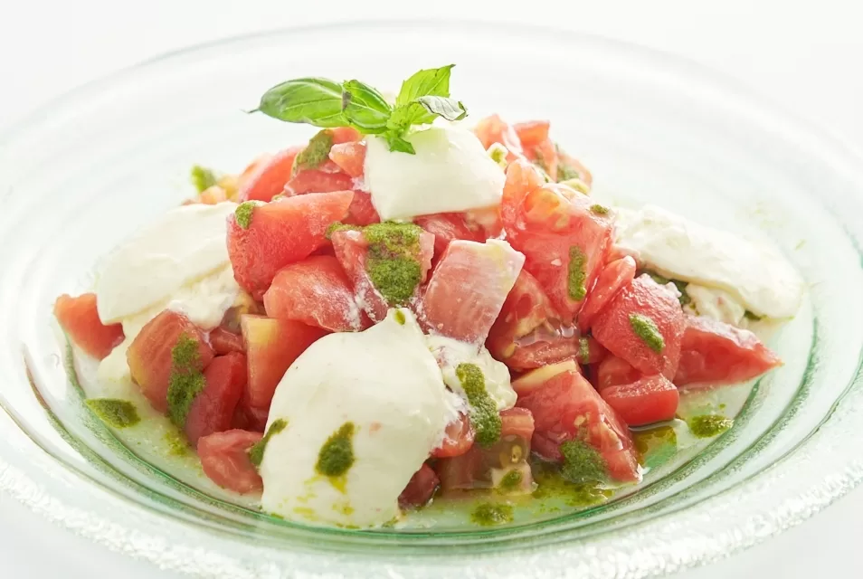 Insalata caprese with fresh tomatoes and creamy burrata cheese, drizzled with herb dressing.