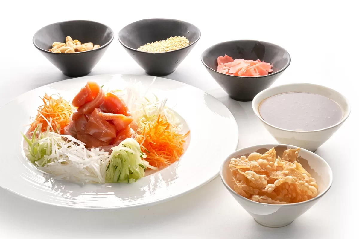 Lo hei with fresh raw salmon, shredded vegetables, and crunchy toppings served with sauce.