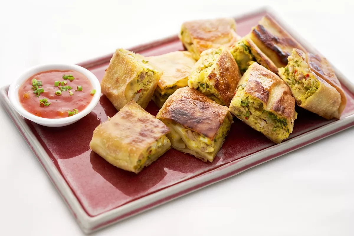 Martabak stuffed with egg, chicken, and vegetables, cut into pieces and served with dipping sauce.