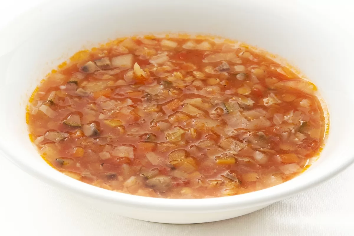 Minestrone soup with chopped vegetables in a rich tomato broth served in a white bowl.