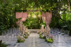 Garden wedding ceremony setup at Moonlight Garden with a floral arch and clear chairs along a decorated aisle.