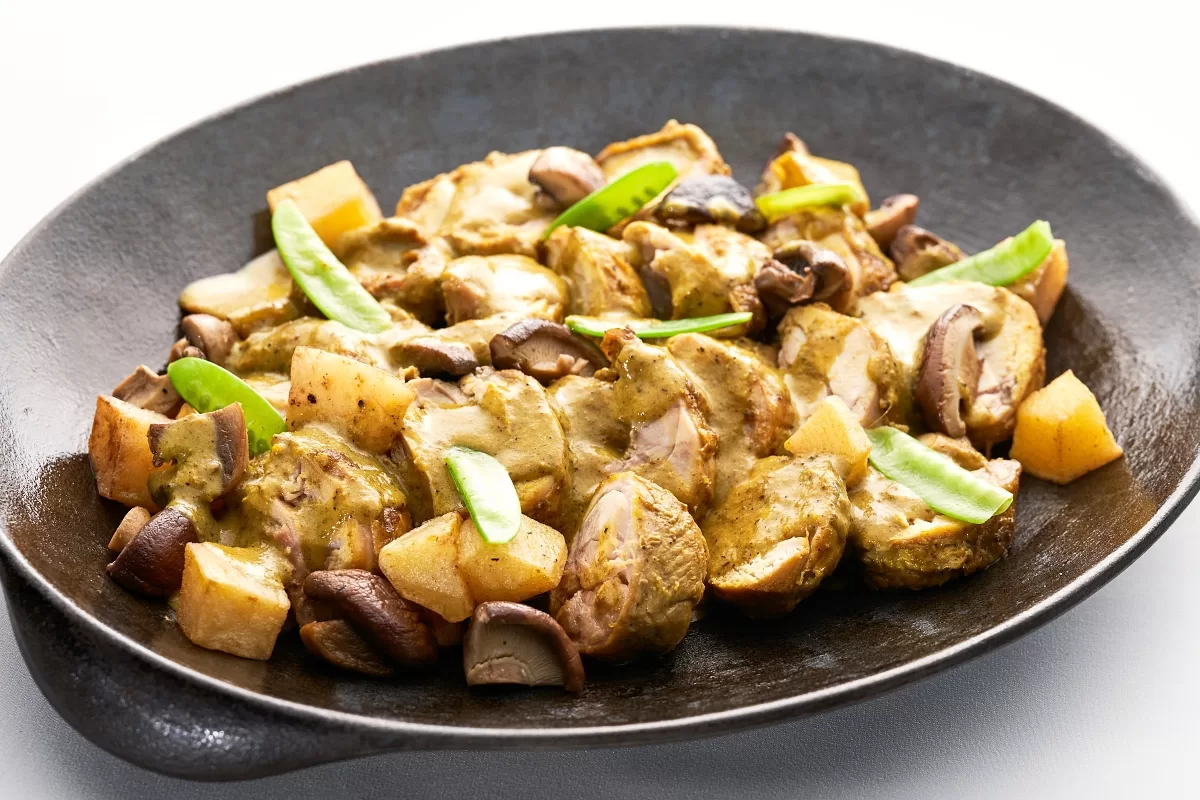 Opor ayam with chicken, potatoes, and mushrooms, served on a plate with green garnish.
