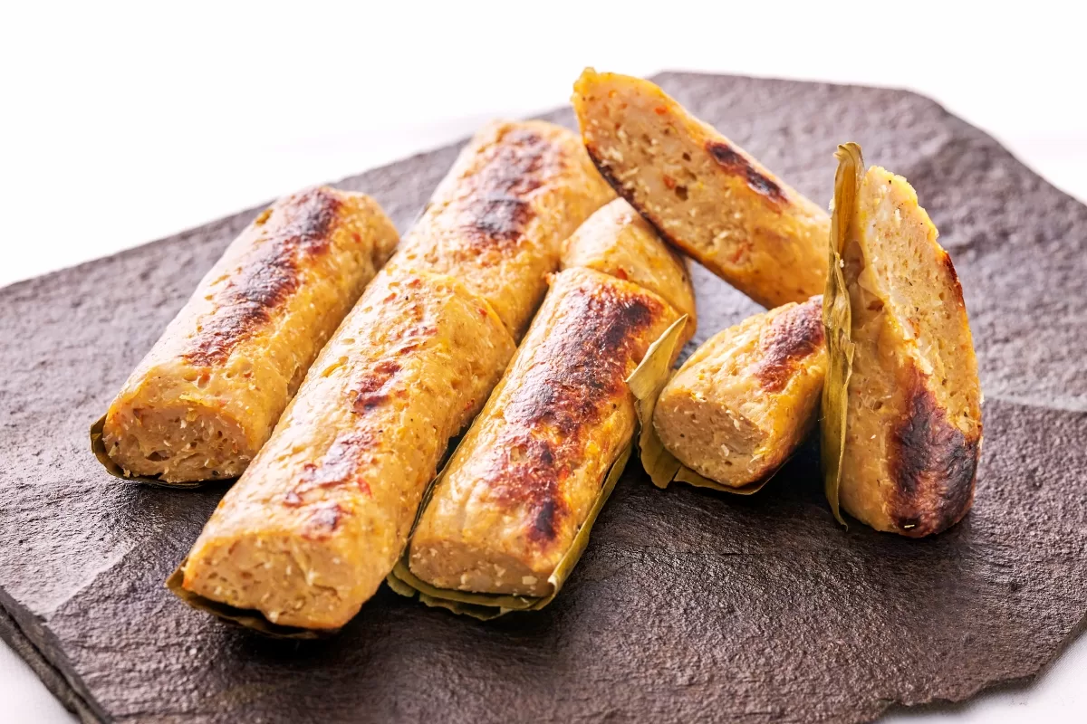 Otak otak, grilled fish paste with a lightly charred surface, served on a stone plate.