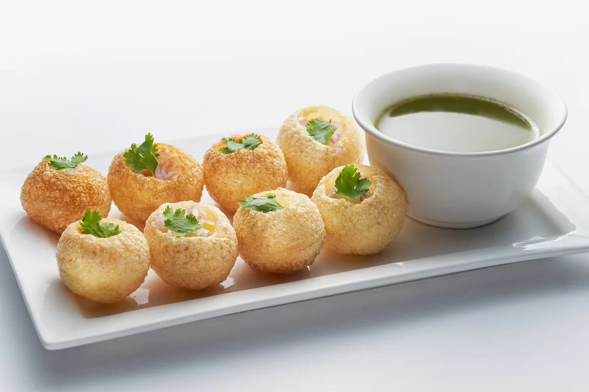 Pani puri with crispy shells filled and garnished with cilantro, served with spiced herbal water.