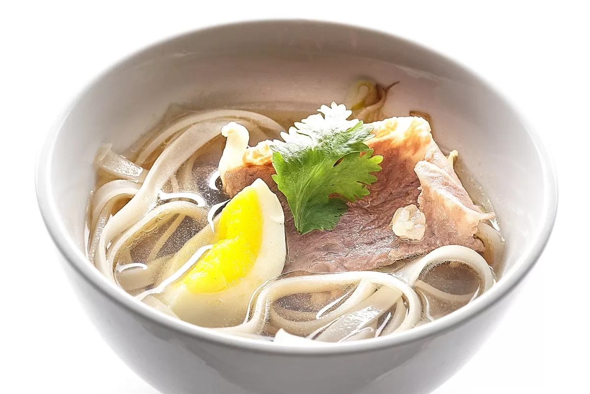 Pho with beef slices, rice noodles, egg, and garnish in a clear savory broth.