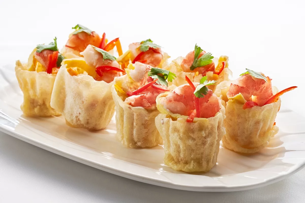 Pie tee with crispy pastry shells filled with savory vegetables and prawns, topped with fresh garnish.