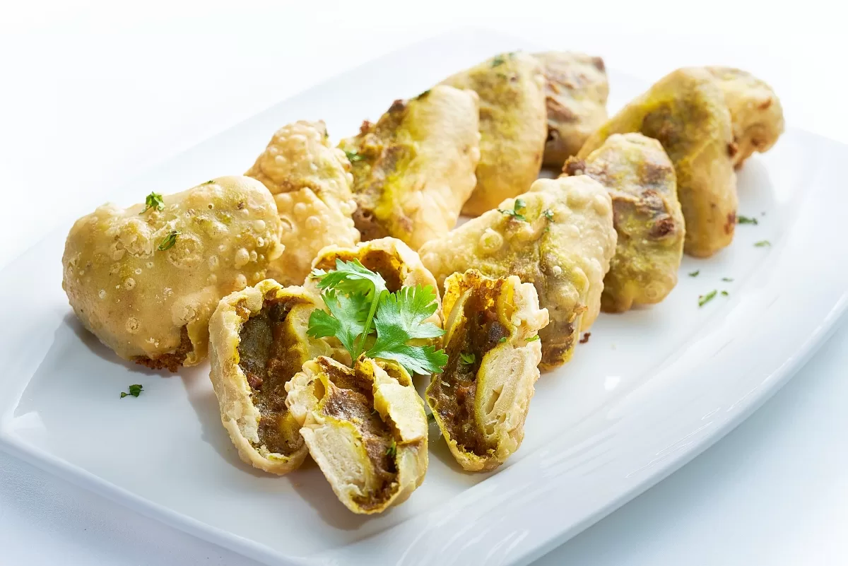 Samosas with golden, crispy pastry filled with spiced potatoes, garnished with coriander.