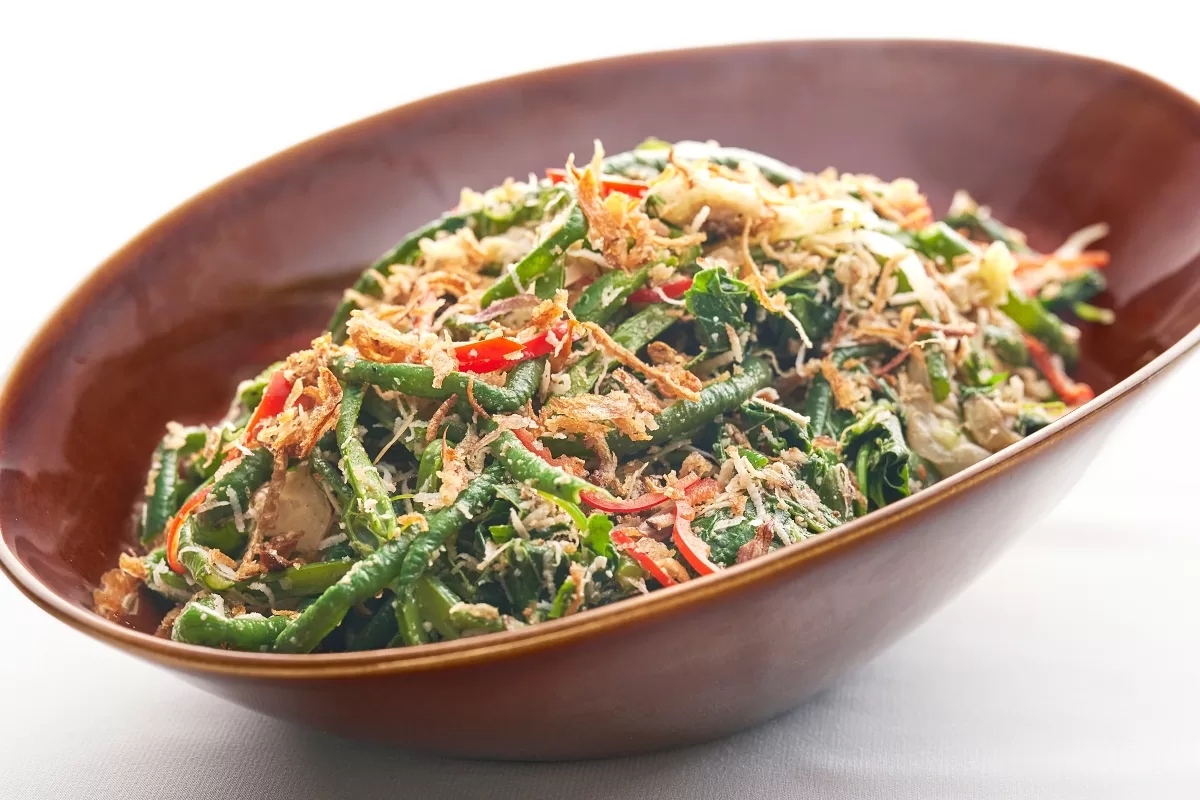 Sayur urap with blanched vegetables and grated coconut mixed with house-blended spices, served in a bowl.