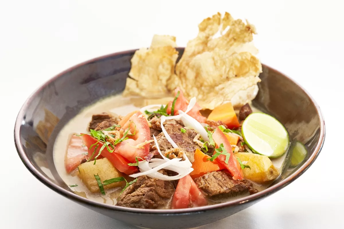 Soto Betawi with beef, tomatoes, potatoes, and crackers, served in a coconut milk broth.