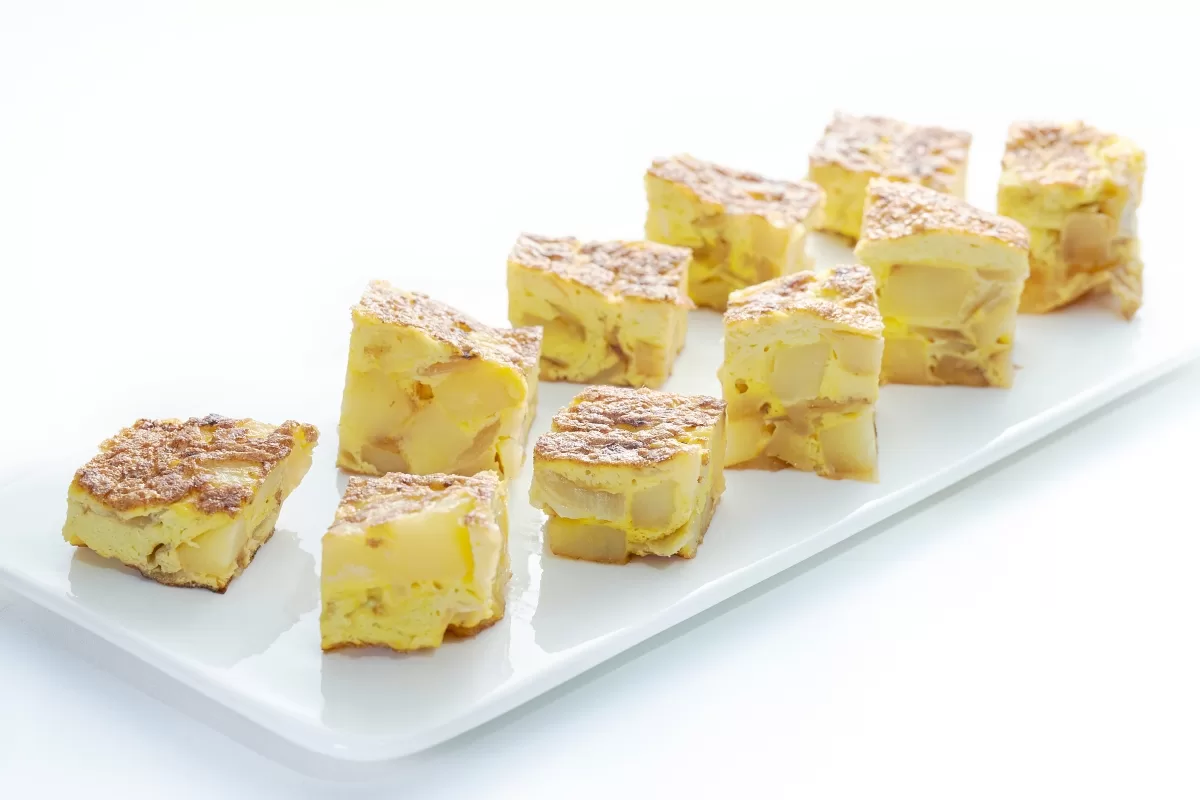 Spanish omelet cut into cubes, with eggs and potatoes, served on a white plate.