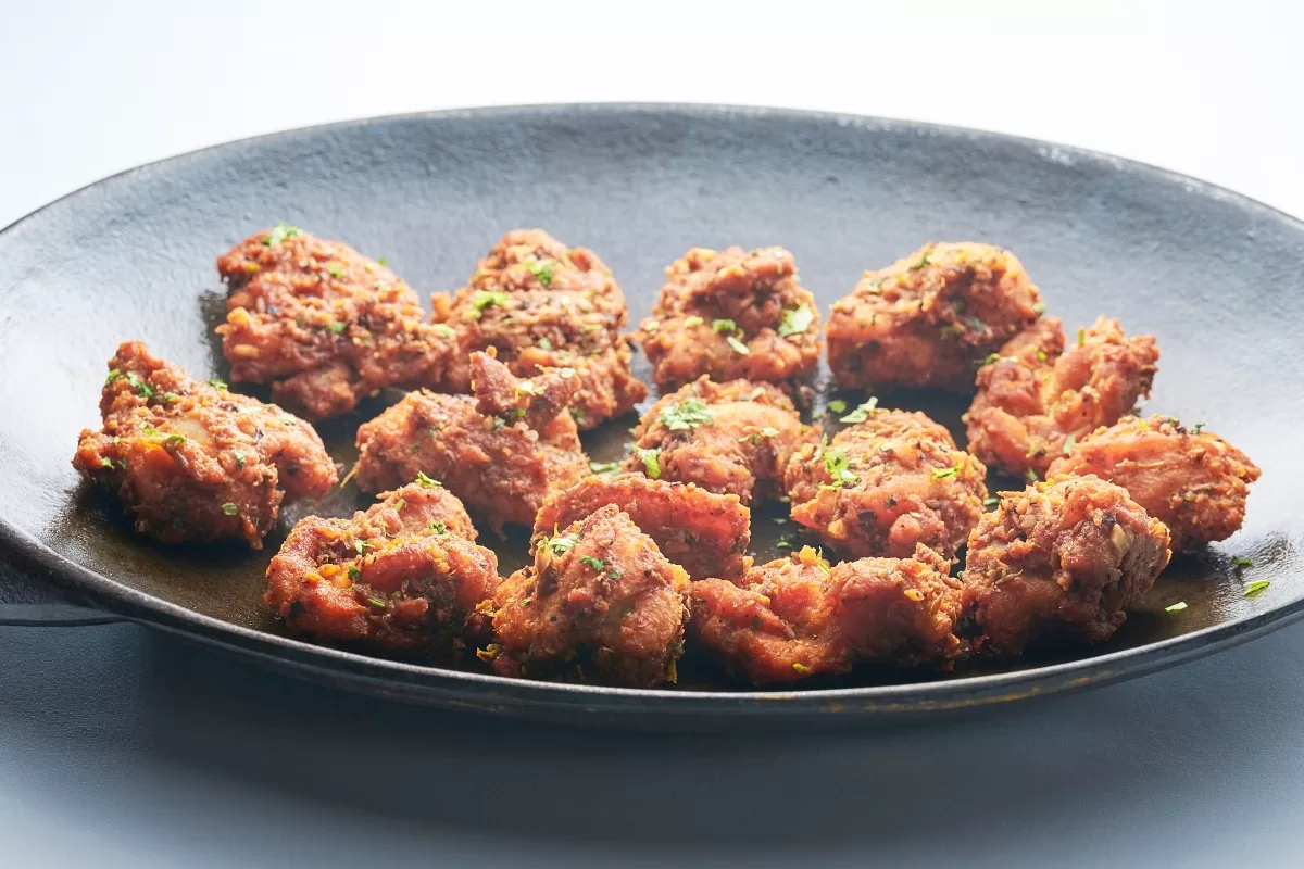 Chicken 65, made with crispy fried chicken pieces coated in house-blend spices and sprinkled with herbs as a garnish.