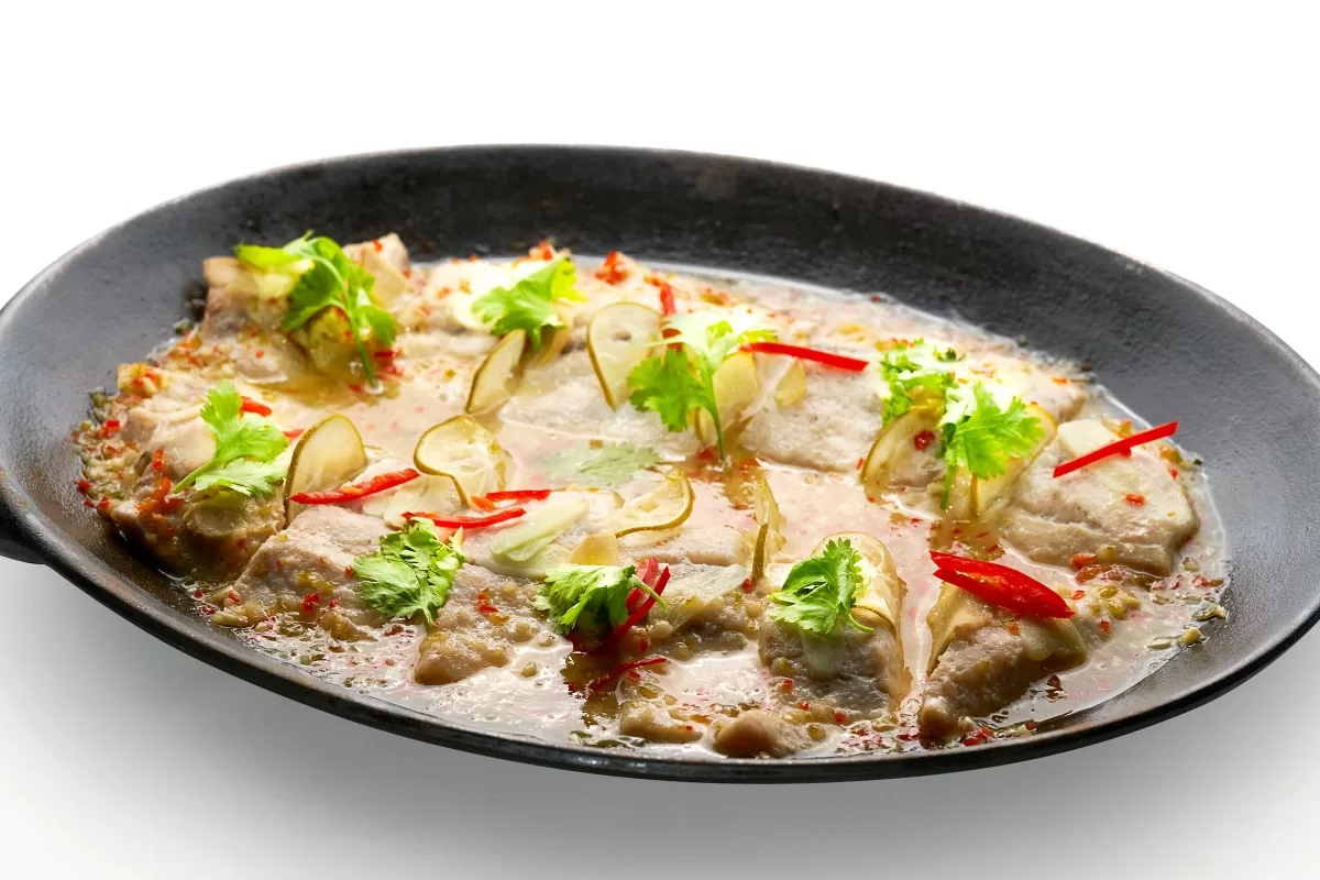 Steamed fish in a tangy, spicy broth with lime juice, garnished with cilantro and red chili.