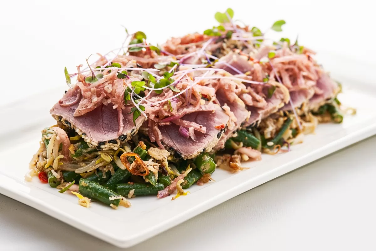 Tuna tataki with seared slices, sambal, and mixed vegetables topped with fresh sprouts.