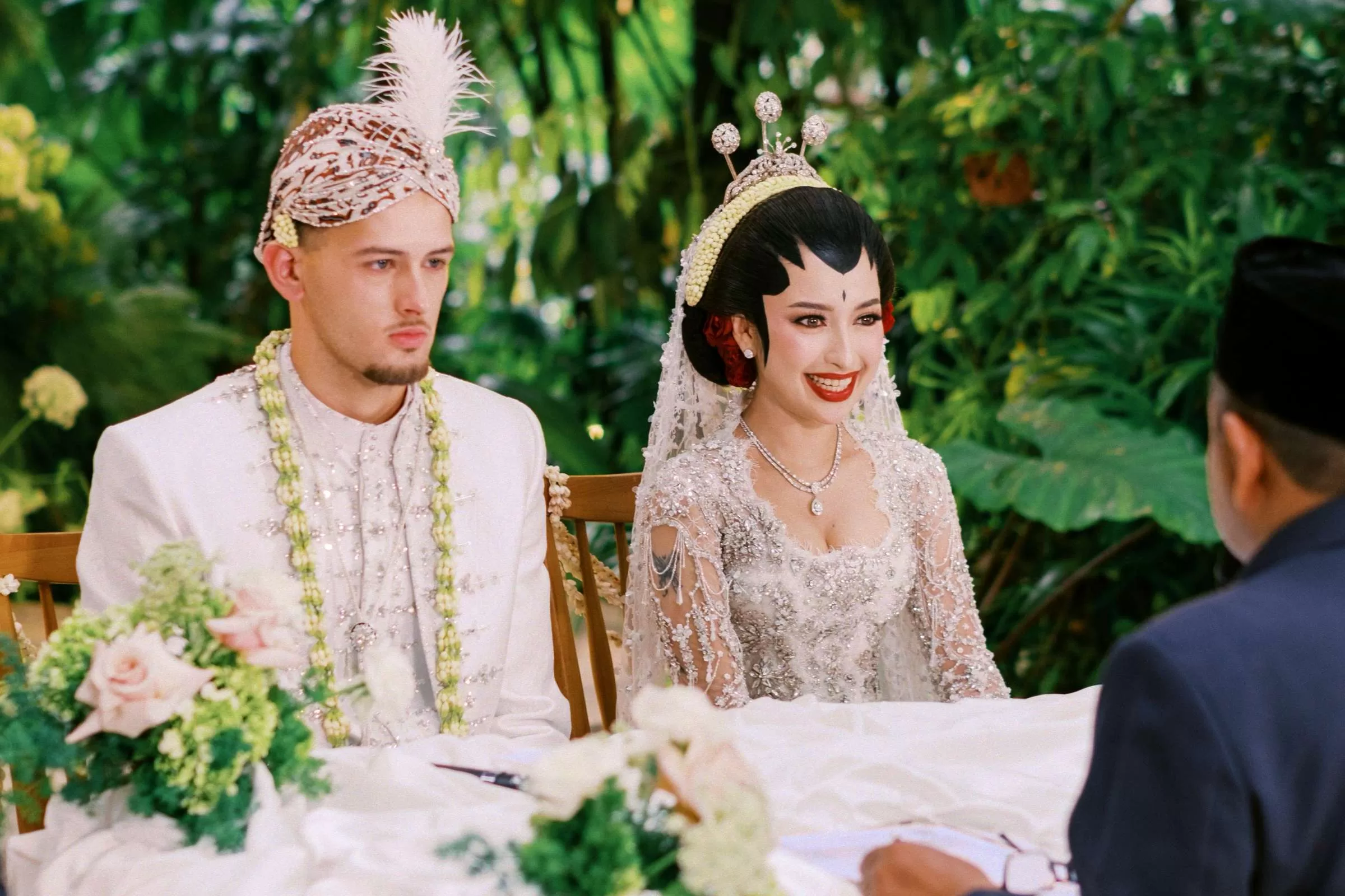 The bride and the groom in traditional wedding attire, sitting in front of the officiant during a Muslim wedding ceremony.