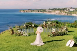Bride standing at Bayuh Sabbha's clifftop wedding venue overlooking the ocean, surrounded by floral ceremony arrangements.